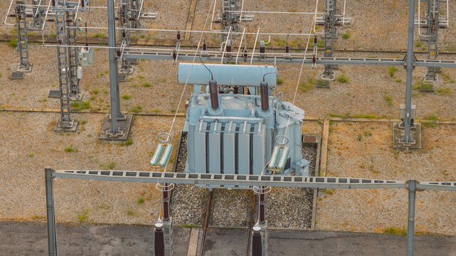 Aerial view of a high-voltage electrical transformer and switching equipment inside a modern power substation with gravel ground and metal support structures in Valence, Auvergne-Rhone-Alpes, France.