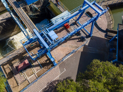 Aerial view of a blue gantry crane structure spanning a waterway at a dam facility in Banyumas Regency, Central Java, Indonesia.