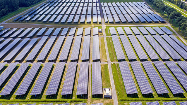 Aerial view of a large solar farm with rows of photovoltaic panels installed on green fields in Biddinghuizen, Flevoland, Netherlands.