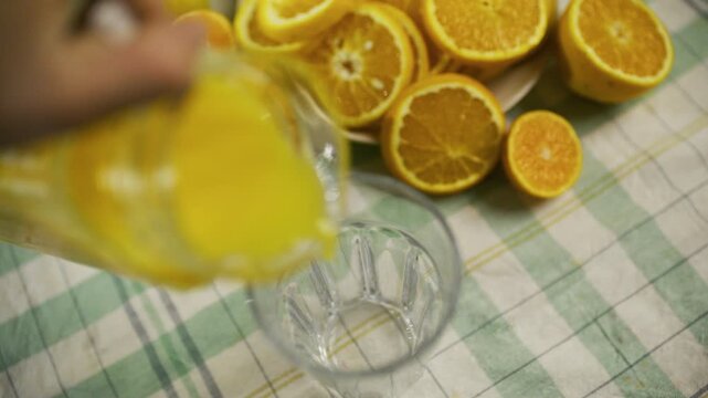 Cinematic slow motion high shot of person pouring juice into glass cup near orange slices