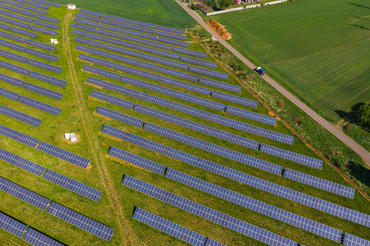 Aerial view of a large solar farm with rows of photovoltaic panels installed on green grass fields, with a road and surrounding agricultural landscape in Kyjov, South Moravian Region, Czechia.