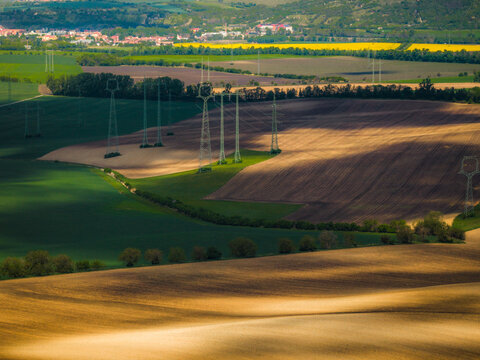 Aerial view of rolling agricultural fields with power lines casting shadows across the landscape in Brno, South Moravian Region, Czechia.