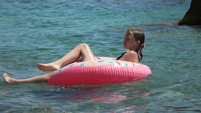Girl swimming pool, child relaxing on donut float in tropical ocean water during summer vacation, happy kid enjoying seaside holidays at beach