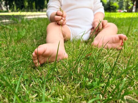 Baby sitting on lush green grass in a park with bare feet. child under one year old