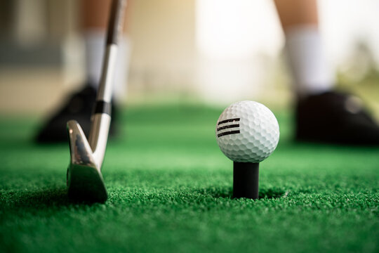 Golf Ball close-up on a tee beside an iron club at a driving range, capturing the moment before a golfer practices a shot on artificial turf