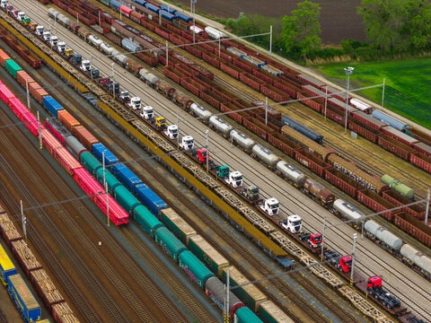 Aerial view of a busy railway yard with freight trains, including flatbed rail cars loaded with semi-trucks, cargo containers, and tankers, in Breclav, South Moravian Region, Czechia.