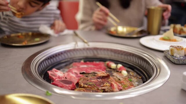 People enjoying traditional korean barbecue dinner, grilling marinated beef and ribs on a tabletop stove while eating with chopsticks in a specialty restaurant