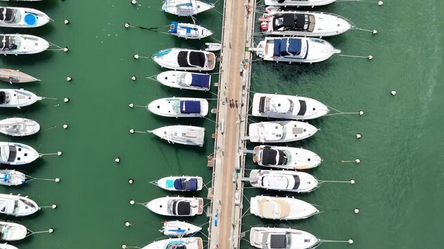 Aerial top-down drone footage of luxury yachts and sailboats moored in a marina, creating a clean geometric pattern on emerald green water.