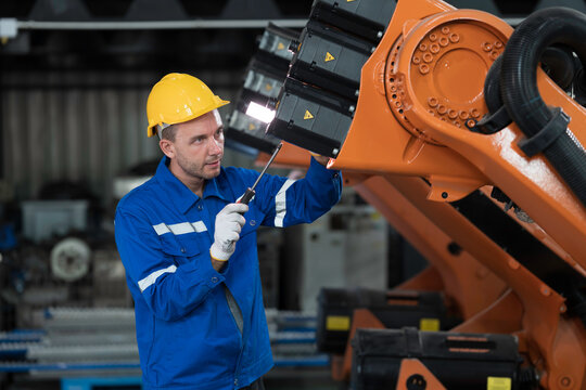 Portrait of male engineer wearing uniform, hard hat and gloves repair automatic robotic arm for welding. Male technician inspecting automatic welding robot arm machine with hand tools