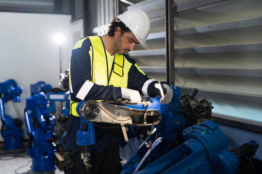 Male engineer wearing uniform, white hard hat and gloves repair automatic robotic arm for welding. Male technician inspecting quality automatic welding robot arm machine with hand tools