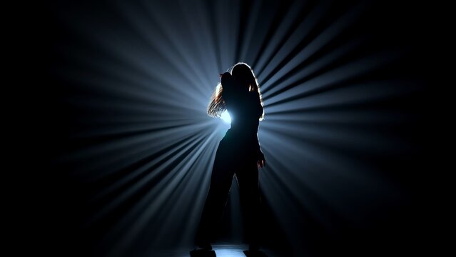 Silhouette of a female dancer performing on a dark stage, back lit by dramatic volumetric light rays with copy space. Concepts related to dance, self discovery, album covers, singles, or podcasts