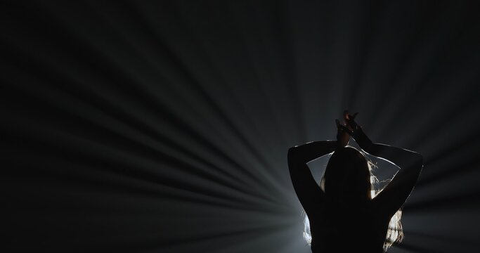 Silhouette of a female dancer performing on a dark stage, back lit by dramatic volumetric light rays with copy space. Concepts related to dance, self discovery, album covers, singles, or podcasts