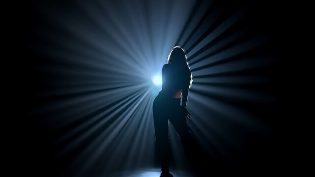 Silhouette of a female dancer performing on a dark stage, back lit by dramatic volumetric light rays with copy space. Concepts related to dance, self discovery, album covers, singles, or podcasts