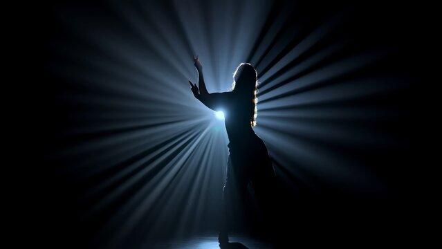 Silhouette of a female dancer performing on a dark stage, back lit by dramatic volumetric light rays with copy space. Concepts related to dance, self discovery, album covers, singles, or podcasts