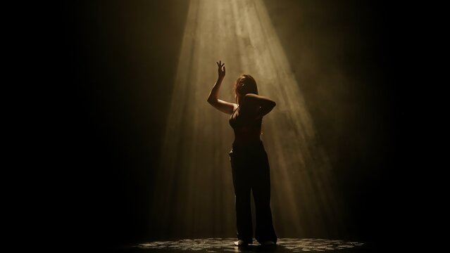 Woman dancing under warm golden spotlight on a smoky stage. Concept of creative backdrop template for music album cover, theater poster and artistic dance promotion.