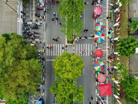 Aerial view of Car Free Day with people walking, colorful umbrellas, lush trees, and motorcycles parked along the street in Samarinda, Kalimantan Timur, Indonesia.