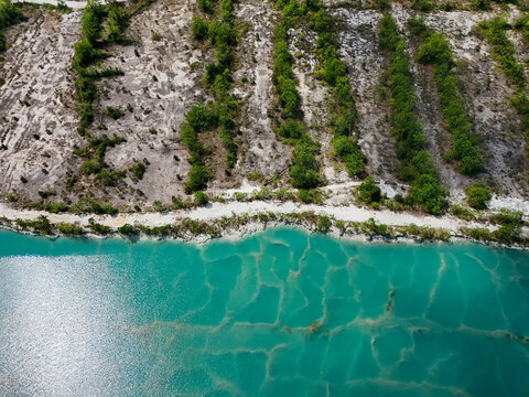 Aerial view of a turquoise lake with patterns on the sandy bottom, bordered by a white shoreline and rows of green trees in Banjar Regency, South Kalimantan, Indonesia.