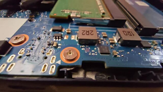 Macro close-up of a laptop motherboard showing surface mount power inductors marked 2R2 and 1R0, microchips, and electronic components during repair