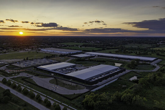 Aerial view of a modern data center complex surrounded by green fields and trees during a vibrant sunset in Hoffman Estates, Illinois, United States.