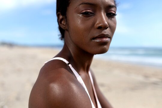 Person on a beach with a tear on their cheek, looking contemplative.