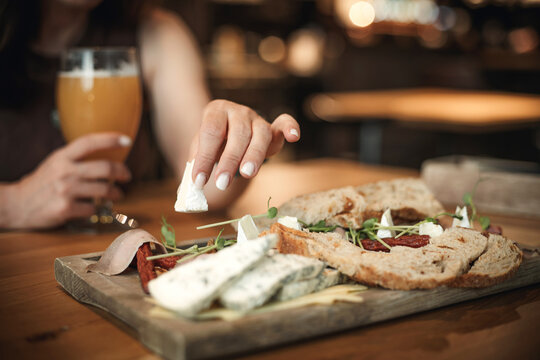 Girl Enjoying Cheese And Wheat Beer From A Snack Board With Sausages At A Pub Table
