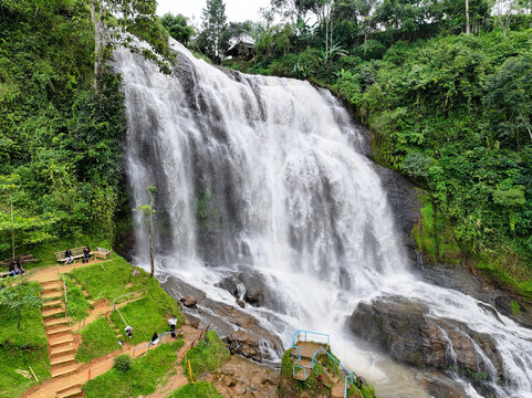 Aerial view of Curug Cikondang waterfall cascading over dark rocks surrounded by lush green vegetation and trees in Campaka, West Java, Indonesia.