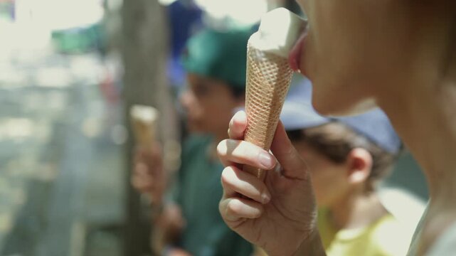 Detailed side-view shot of a woman's hand holding a wafer cone with vanilla ice cream. As she joyfully licks the refreshing dessert on a hot