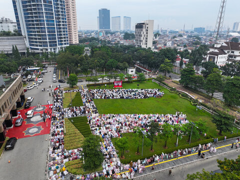 Aerial view of the West Jakarta Mayor office grounds filled with a large crowd gathered for outdoor prayers on a green lawn surrounded by urban buildings in Kembangan, Jakarta, Indonesia.