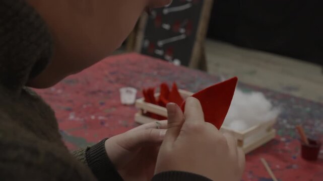 A nine year old girl makes a handmade Christmas elf craft using wood and red felt during a workshop in Santa Claus Village, Rovaniemi, Finland