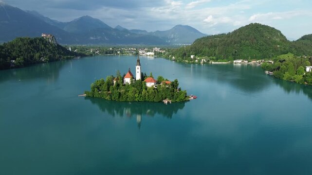 Aerial drone view of Bled Island on Lake Bled, Slovenia, featuring the iconic Church of the Assumption surrounded by turquoise water and alpine mountains.