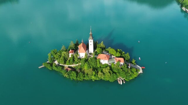 Top down drone view of Bled Island on Lake Bled, Slovenia, featuring the iconic Church of the Assumption surrounded by turquoise water and lush forest.
