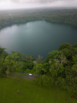 Aerial view of Laguna Hule, a volcanic crater lake surrounded by dense tropical rainforest and lush greenery under a cloudy sky in Costa Rica.