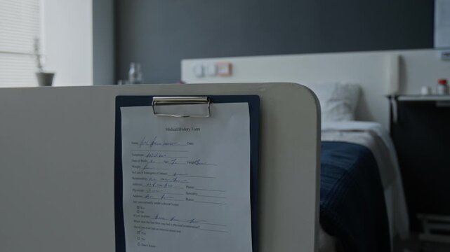Medical history form hanging on clipboard at foot of empty hospital bed in clinic room. Clip for healthcare marketing, medical insurance promos, or clinical services advertising