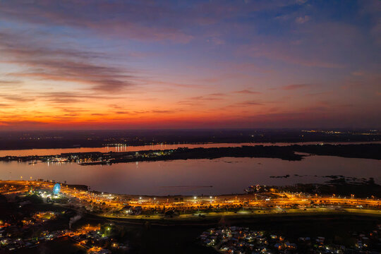 Aerial view of Costanera Norte at sunset with city lights illuminating the waterfront, a ferris wheel, and the Paraguay River in Asuncion, Asuncion, Paraguay.