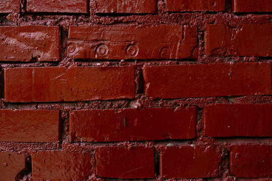 Glossy red painted brick wall with mortar texture and paint drips
