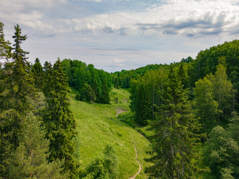 Aerial view of Hantala Hollows featuring lush green meadows, dense pine and spruce forests, and a winding dirt path under a cloudy sky in Hantala, Varsinais-Suomi, Finland.