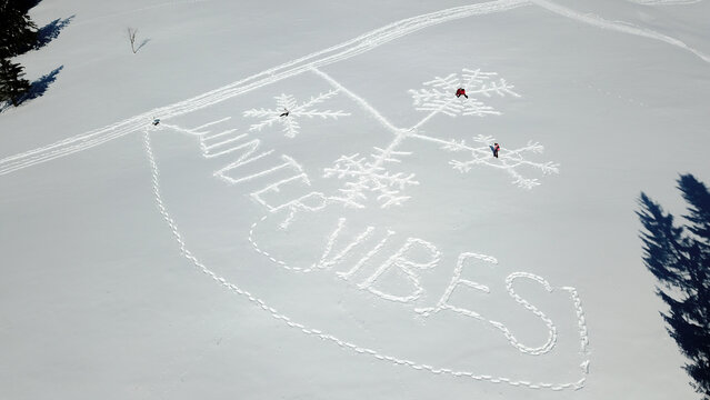 Aerial view of the words Winter Vibes written in the snow with snowflake patterns and people standing on a snowy field in Mijoux, Auvergne-Rhone-Alpes, France.
