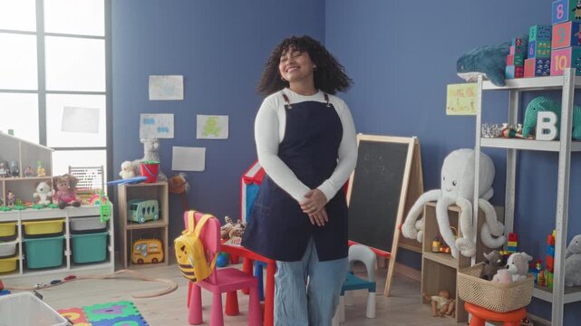 Woman teacher brunette reaching for red maraca on shelf among plush octopus and blocks in kindergarten classroom building; play learning joy.