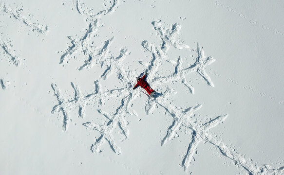 Aerial view of a person in a red suit lying in the snow to create a large snowflake pattern in Mijoux, Auvergne-Rhone-Alpes, France.