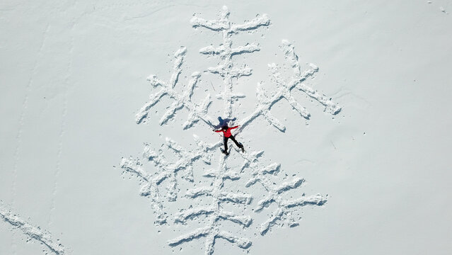 Aerial view of a person in a red jacket lying in the snow forming a large snowflake pattern in the mountains of Mijoux, Auvergne-Rhone-Alpes, France.