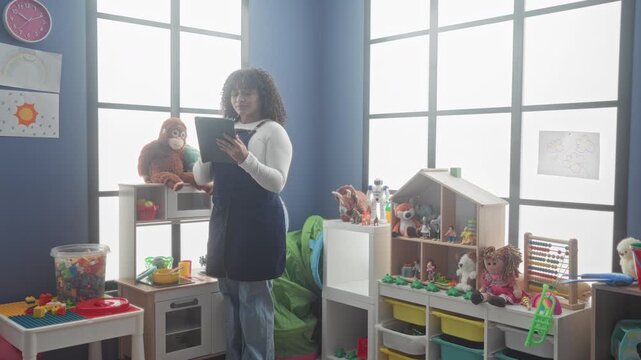 Woman teacher holding tablet and scanning notes while standing in a school building, surrounded by toys and shelves; nurture calm.