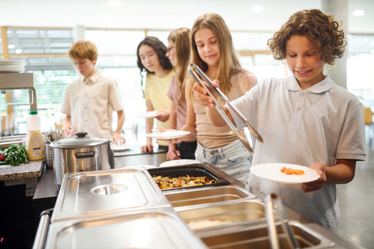 School students serving lunch in a cafeteria while waiting in line