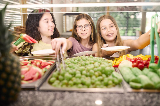 Group of girls selecting fresh fruits in a school cafeteria setting
