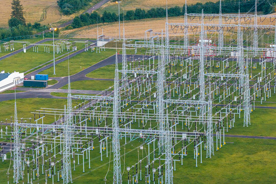 Aerial view of an electrical substation featuring complex metal power structures and high-voltage lines set amidst green fields in Poland.