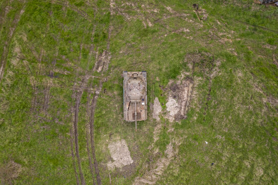 Aerial view of an abandoned military tank sitting in a grassy field with visible tire tracks and muddy patches in Belgium.