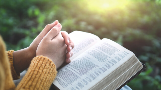 An open Bible and praying hands in natural light symbolize peaceful devotion, hope, biblical meditation, spiritual renewal, and a faithful beginning to each day.