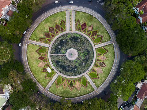 Aerial view of Alun Alun Tugu Malang featuring a circular park with a central pond, fountains, and lotus-shaped garden beds surrounded by lush trees in Malang, East Java, Indonesia.