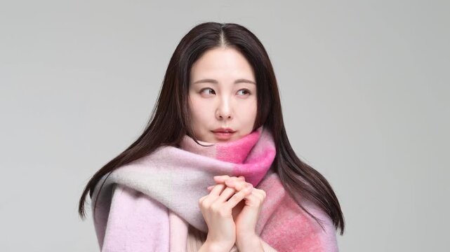 グレー背景の室内でマフラーに包まりながら笑顔を見せる30代の日本人女性