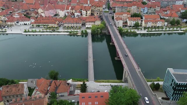Aerial drone view of the Old Bridge over the Drava River leading to the historic center of Maribor with riverside promenade and red tile roofs in Slovenia.