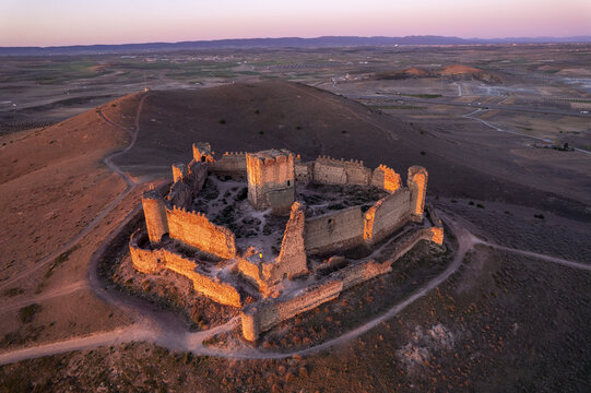 Aerial view of the historic ruins of Castle Almonacid of Toledo perched on a hill during golden hour with the surrounding arid landscape. Almonacid de Toledo, Castilla-La Mancha, Spain.